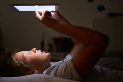 junge liegt im bett und liest auf einem ebook-reader