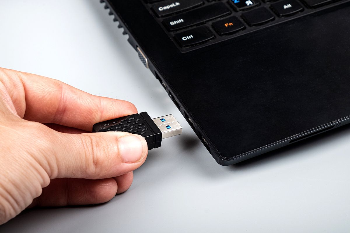 Person steckt kleinen WLAN-Stick in USB-Anschluss am Laptop