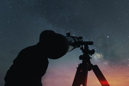 Mann schaut mit Teleskop in Sternenhimmel