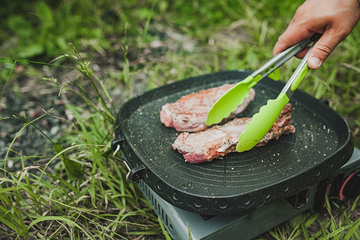 Person grillt Fleisch auf Camping-Gasgrill