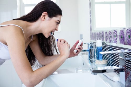 Frau nutzt Smartphone beim Zähneputzen