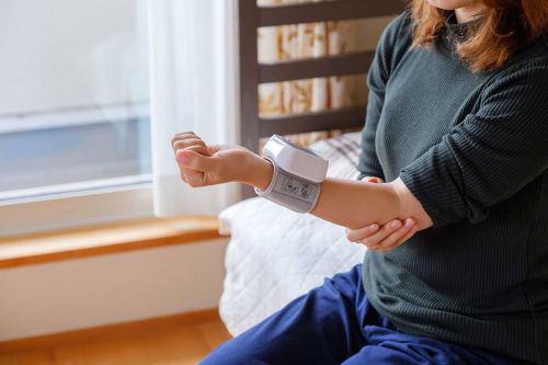Frau mit Handgelenk-Blutdruckmessgerät auf Bett