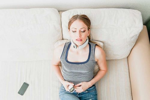 junge Frau auf Sofa nutzt Nackenmassagererät