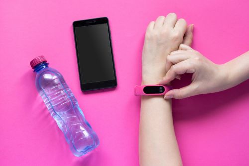 schrittzaehler am handgelenk auf pinkem hintergrund, wasserflasche und smartphone daneben
