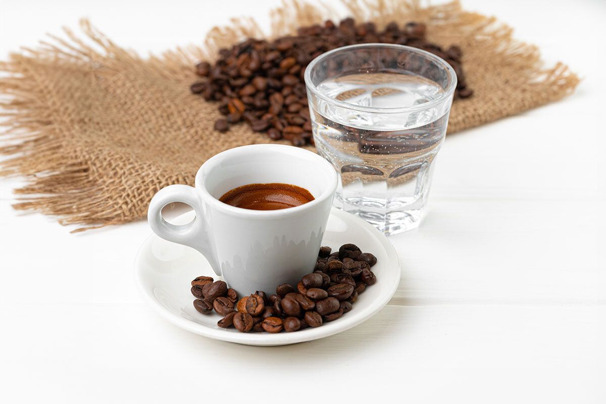 Frischer Espresso mit Espresso-Bohnen in Untertasse und einem Glas Wasser