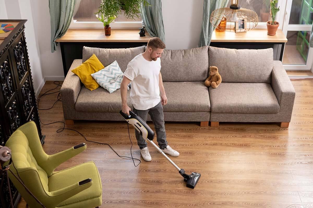 Mann reinigt Wohnzimmer mit Stabstaubsauger
