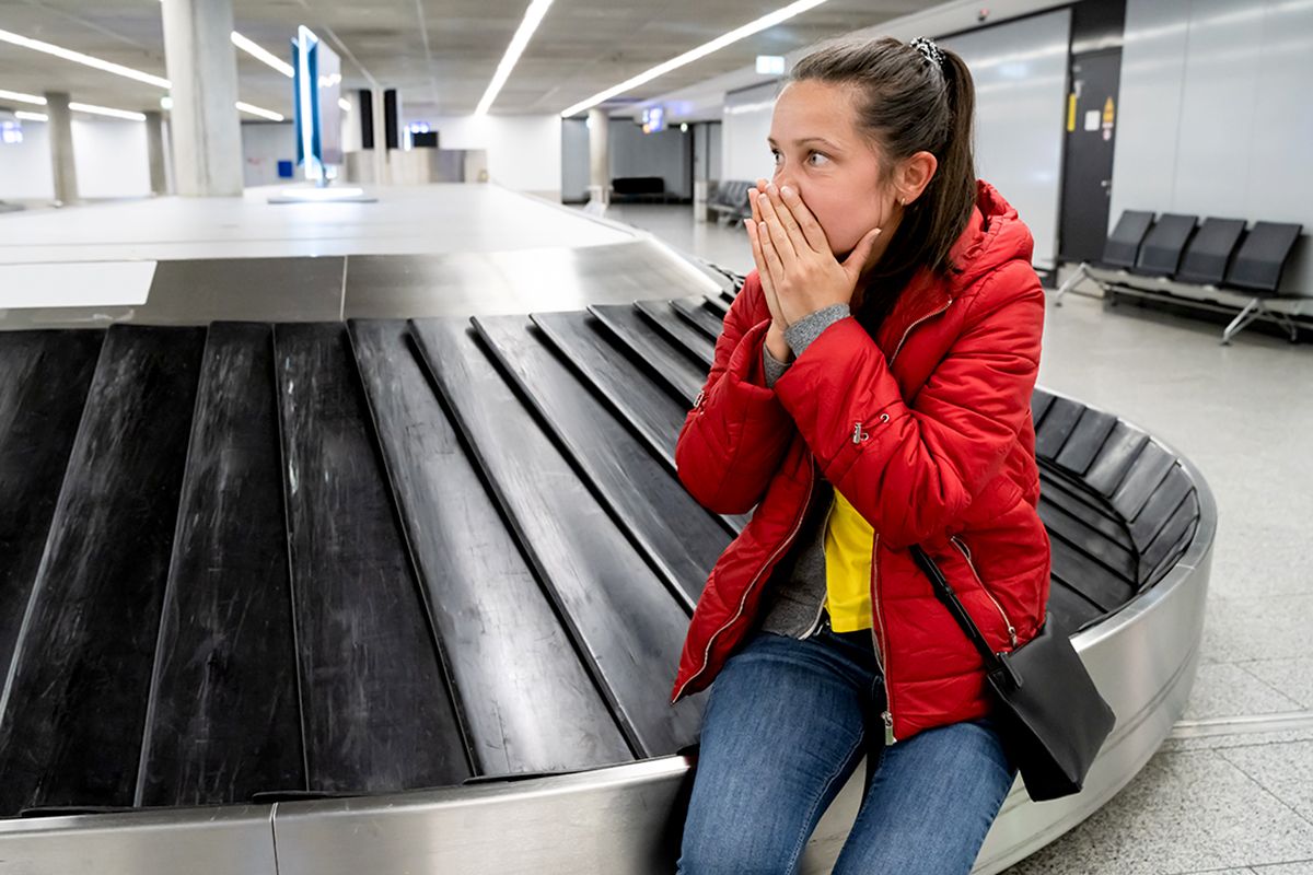 Frau sitzt schockiert am leeren Gepäckband.