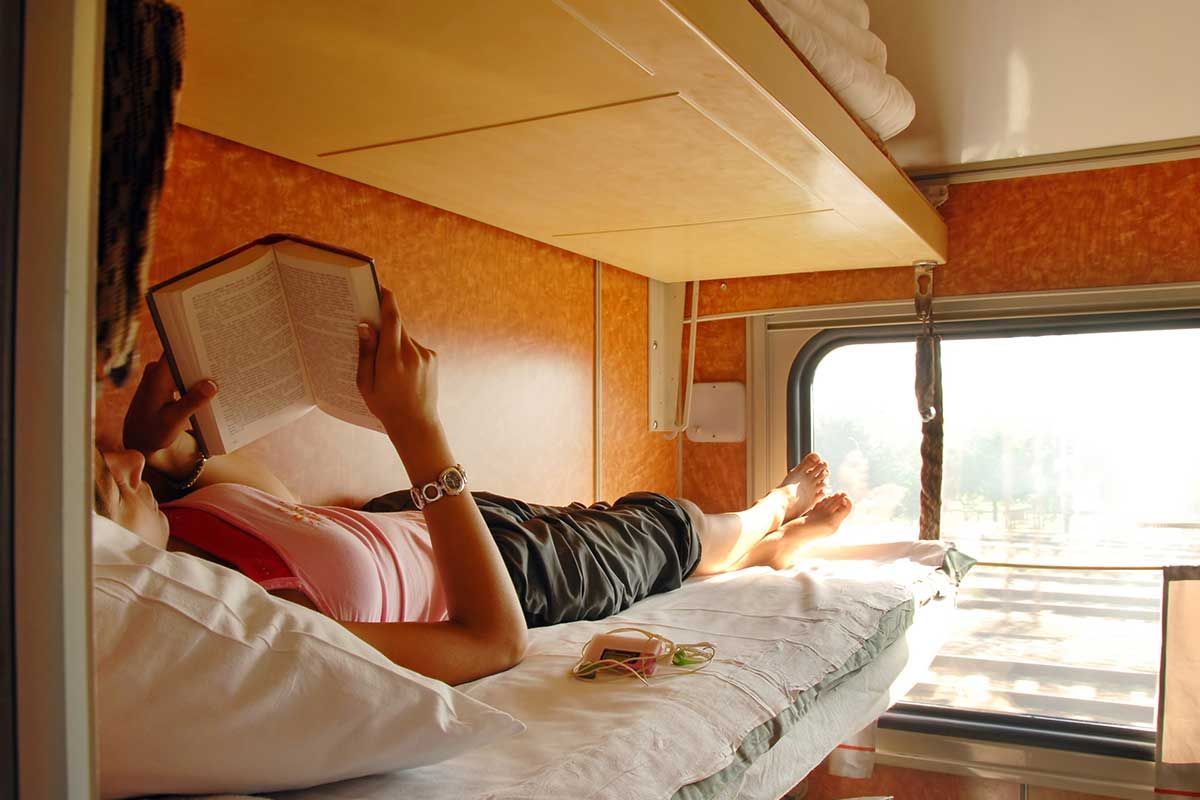 Frau liegt im Zug auf Bett und liest Buch