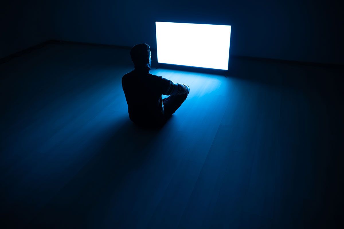 Person sitzt vor Fernseher in dunklem Raum