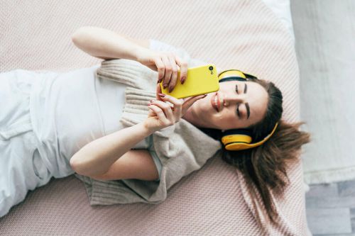 Frau liegt auf Bett mit Handy und Kopfhörern